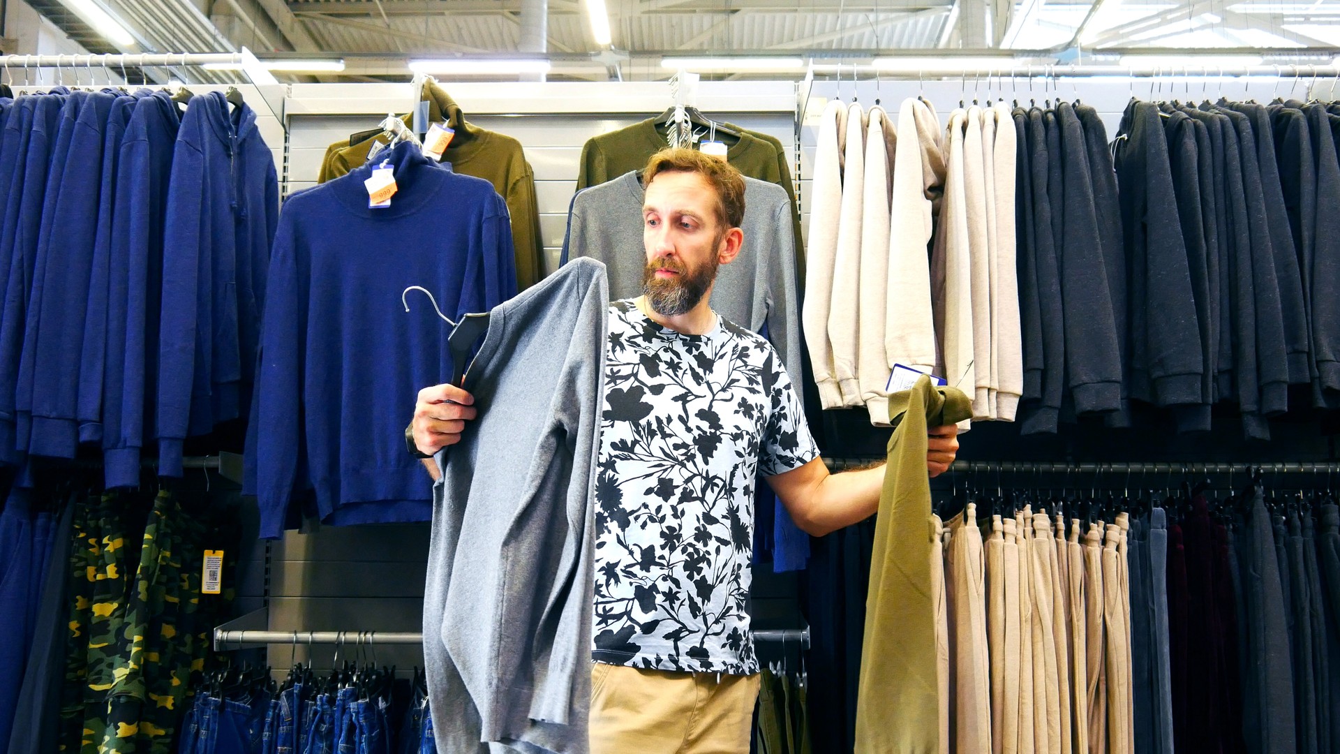 A male buyer holding pullover and turtleneck wondering what to choose